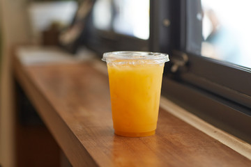 DISPOSABLE PLASTIC CUP DRINKS , plastic cup of tea for takeaway place on wood counter table in cafeteria  besides blur windows background. Close up and selective focus