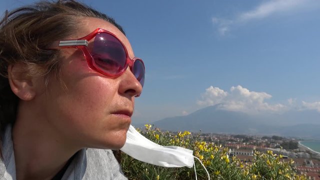Fethiye, Turkey - 27d of March 2020: 4K Profile of woman taking off medical mask against panoramic view
