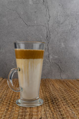Iced Dalgona Coffee, a trendy fluffy creamy whipped coffee in a tall glass over wooden background.