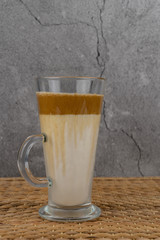 Iced Dalgona Coffee, a trendy fluffy creamy whipped coffee in a tall glass over wooden background.