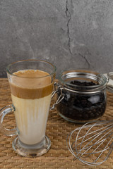 Iced Dalgona Coffee, a trendy fluffy creamy whipped coffee in a tall glass over wooden background.
