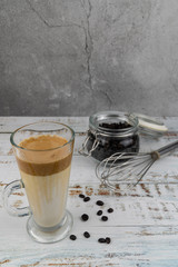 Iced Dalgona Coffee, a trendy fluffy creamy whipped coffee in a tall glass over wooden background.