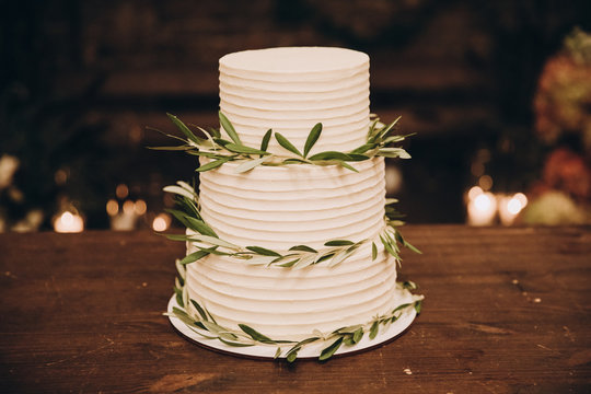 White wedding cake decorated with green leaves and stands on a wooden table in the loft