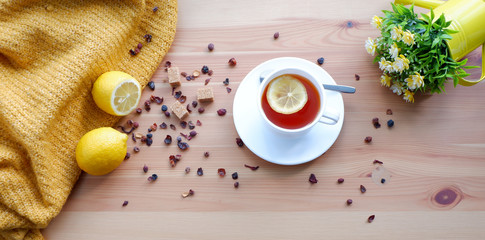 tea with lemons and a watering can with flowers on a wooden table. Beautiful background. Mockup