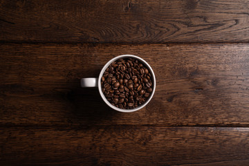 Zdjęcie ziaren kawy w białym kubku na drewnianym, brązowym stole