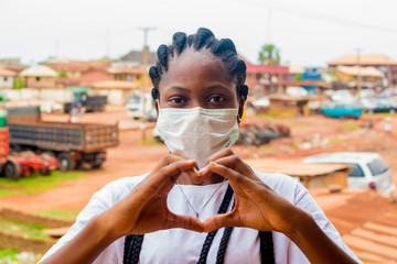 young black beautiful lady wearing a nose mask and giving a love sign with her hand