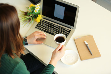 Young woman with a cup of coffee works in the office at the laptop