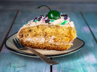 A slice of homemade cake with cream and confectionery decorations served on a small plate with a dessert vintage fork