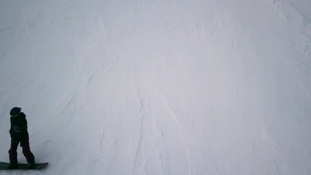 Snowboarder descends from the mountain, aerial shoot. The camera watches the snowboarder who descends from the mountain and then disappears from frame.