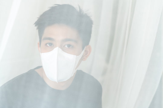 Asian man wearing Face Mask to protect  feeling sick headache and cough because of Coronavirus covid-19 in quarantine room , Quarantine yourself to protect spread Covid-19 Coronavirus