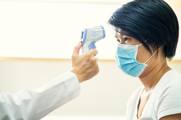 Female doctor check Asian woman body temperature using infrared forehead thermometer (thermometer...