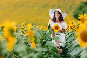 beautiful young woman in a white dress and hat on a field of sunflowers , smiling a beautiful smile,cheerful girl,style, lifestyle , ideal for advertising. selective focus