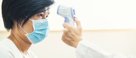 Fototapeta premium Banner of doctor check Asian woman body temperature using infrared forehead thermometer (thermometer gun) for virus symptom at hospital. Corona virus, Covid-19, quarantine or virus outbreak concept