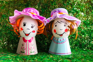 Funny, homemade from chicken eggs and paper young ladies in hats on a green background. Easter card.