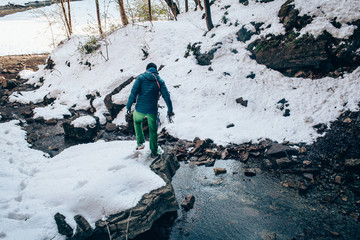 Young male tourist goes down in the mountains near the river in winter. Travel, trekking  and active life concept. Hiking, camping equipment.