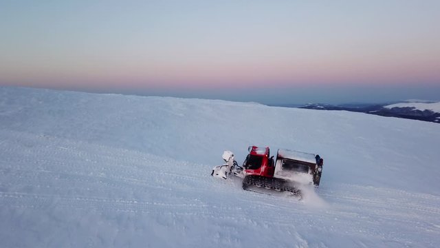Snowcat rises uphill at dawn, aerial shoot. Climbing a snowcat on a mountain against the background of the dawn sky and the moon.