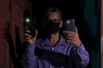 An aged citizen of India is lighting his mobile torches to show fellow citizens about integrity and solidarity towards the nation to fight corona virus together. Indian citizens lifestyle in COVID  