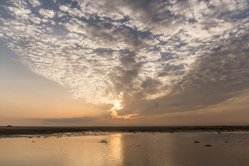 sunset on the beach, sky with orange colors and clouds, sea with small waves