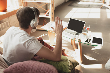 Young man studying at home during online courses for musician, drummer, producer. Getting profession or hobby while isolated, quarantine against coronavirus. Using laptop, smartphone, headphones.