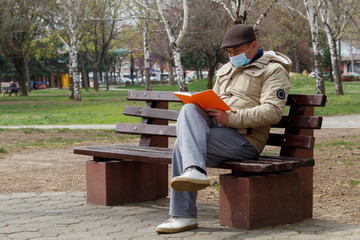 Middle Age Man With Medical Mask Sitting on Bench in Public Park and Reading  a Book