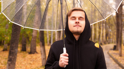Portrait of a young man walking along the autumn park in a rainy day