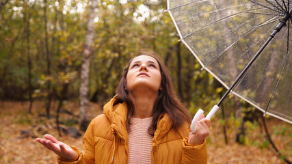 Portrait of a pretty woman holding an umbrella under the rain in autumn park