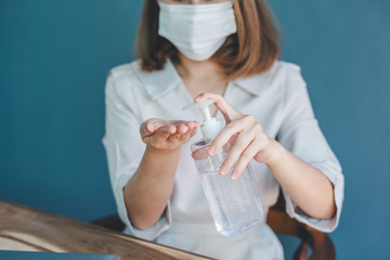 A woman in a white dress carrying an alcohol gel bottle is about to wash her hands to kill bacteria and prevent the spread of the Covid-19 virus in the home office.