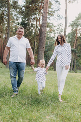 Obraz premium happy Family walking in the park holding hands and smiling. mom, dad and daughter spending time together outdoor on a summer day. selective focus