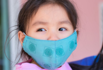 An Asian girl wearing a pink T-shirt stands wearing a sanitary mask.
