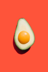 egg yolk in ripe avocado on a red background. 