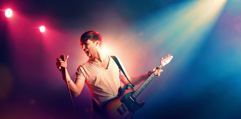 Young male singer performing on a stage and playing the guitar - obrazy, fototapety, plakaty
