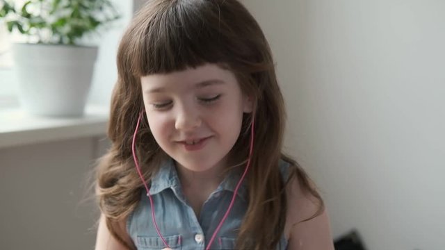 A 6-7 year old girl listens to music with pink headphones and dances at home