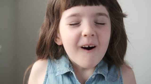 A 6-7 year old girl closes her eyes and imagines, is surprised. Close up.