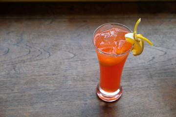 close up one glass of orange cocktail with fruit slice on patterned wooden table. blur background