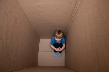 bullied hunched child sitting in a box, seeking for help and refuge from domestic violence in his...