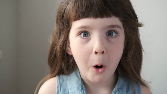 A 6-7 year old girl hatches her eyes and is surprised by what she sees, looks at the camera. Close up.