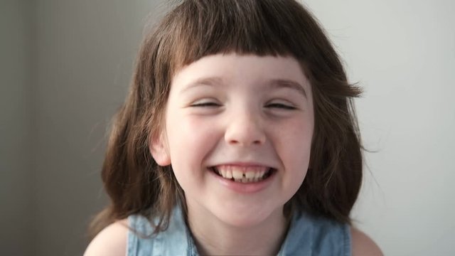 A 6-7 year old girl looks at the camera and laughs. Close up.
