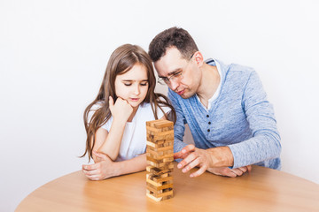 Girl and dad play a game at home, cost a tower of blocks, cubes, jenga, puzzle for brain...