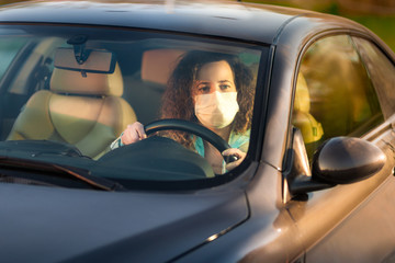 Curly woman driving her car and wearing medical mask in the traffic during covid-19 epidemic