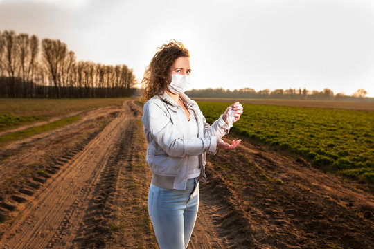 Beautiful casual woman using sanitiser prevention infection on a path near meadow in the nature during covid and wearing medical mask. Many people walking in the nature during quarantine and epidemic.