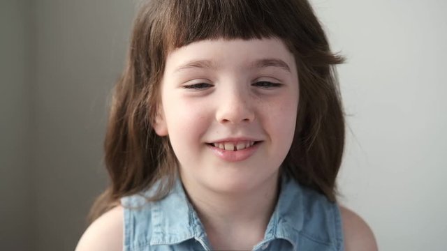 A 6-7 year old girl moves her eyes in a circle and smiles, looking at the camera. Close up.
