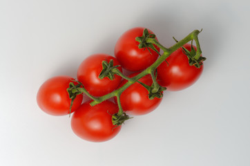 Red cocktail tomatoes on a branch. Light gray background. View from above. Soft shadows.