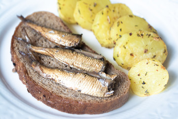 Canned sprats on rye bread served with herb baked potatoes