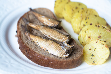 Canned sprats on rye bread served with herb baked potatoes