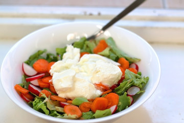 Bowl of salad with lettuce, carrot, radish and cottage cheese, on a rustic, Mediterranean style window. Selective focus.