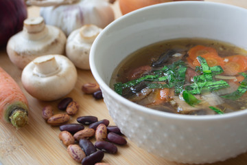 Healthy vegetable and bean soup with its ingredients: carrots, mushrooms, onions, garlic, herbs and kidney beans