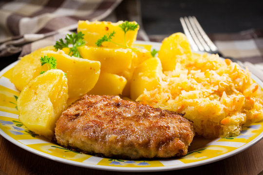 Minced pork cutlet served with potatoes and sauerkraut salad.