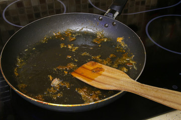 Dirty wooden pan scraper lies in black non-stick frying pan covered with large amount of fat after frying food in the kitchen. The theme of washing dishes after cooking.