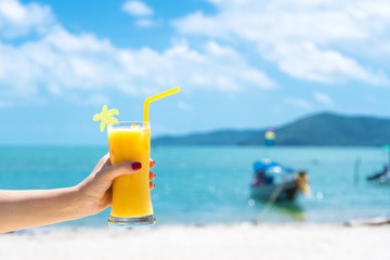 First-person view. Girl holds a glass cup of cold mango fresh on the background of a sandy tropical beach. White sand and a boat. Fairytale vacation in Thailand