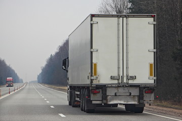 Contemporary white semi truck on empty two-lane road at spring day, international cargo logistics goods delivery